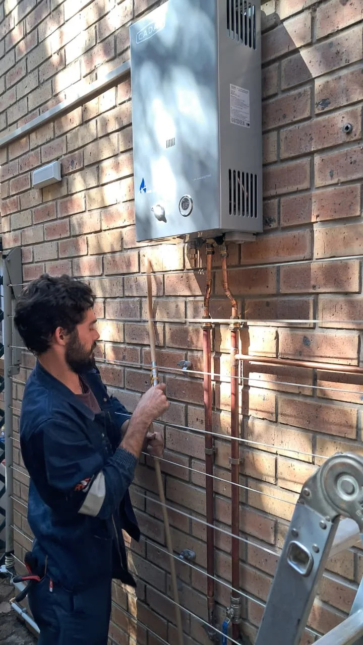 Daimon of GasCraft George installing a Cadac gas geyser with copper pipework on a brick wall in George