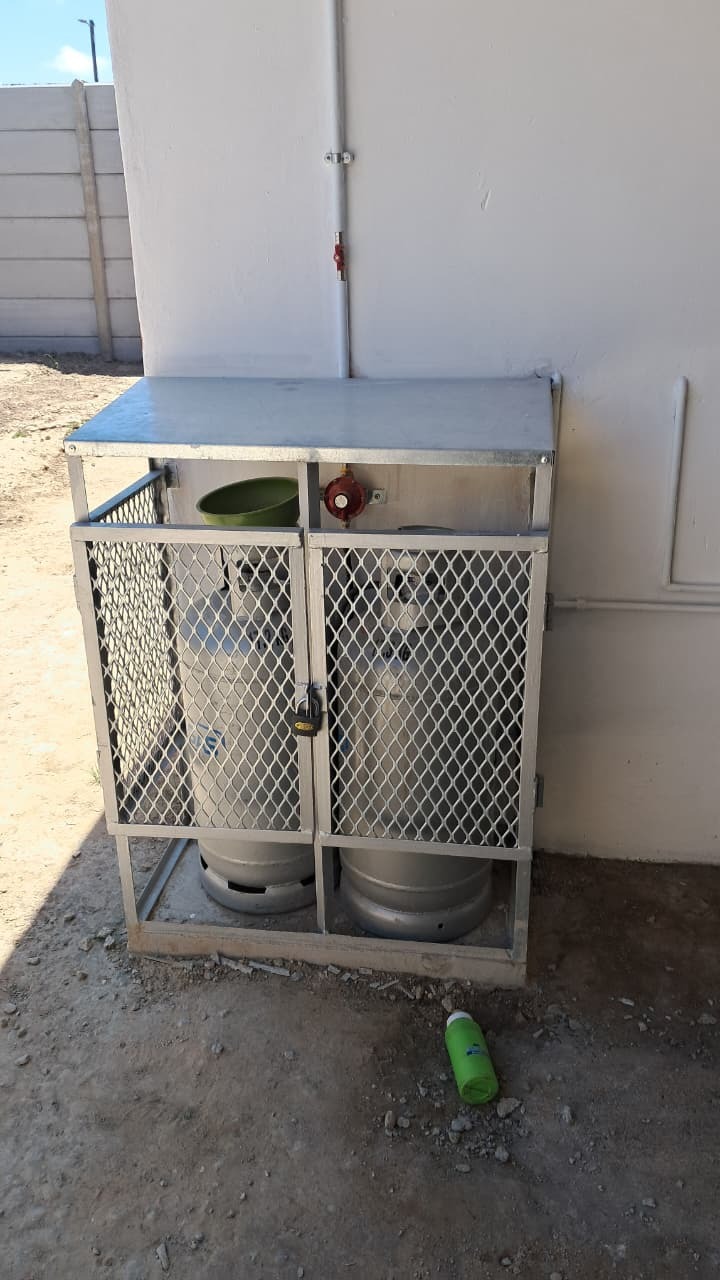Galvanised mesh gas cylinder cage against an exterior wall checked during a gas safety inspection in George