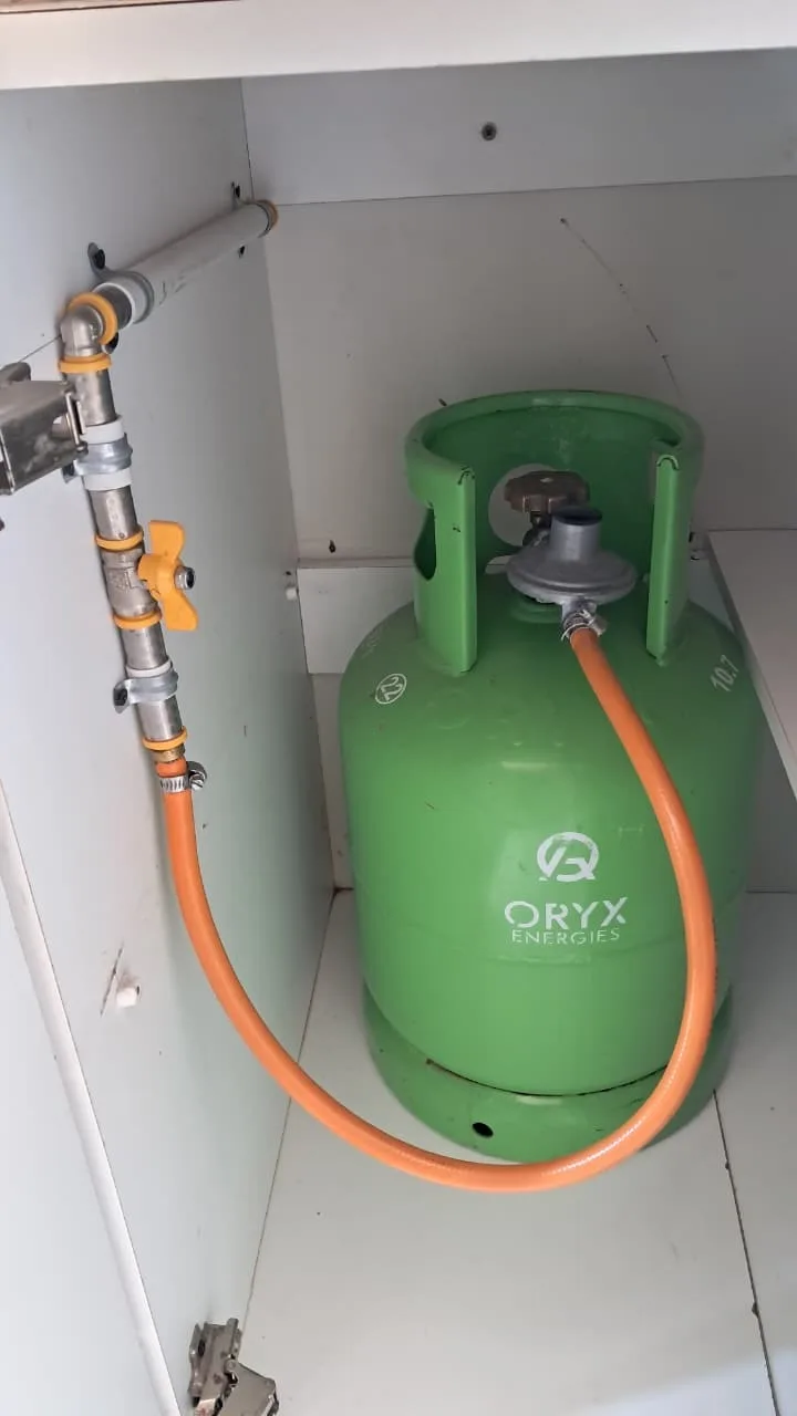 Under-counter gas cylinder installation with regulator and orange hose supplying a gas stove in a George kitchen